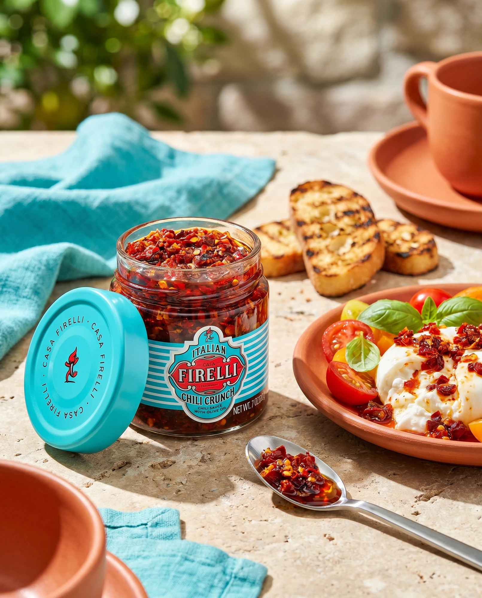 Vasetto di Chili Crunch Casa Firelli accanto a bruschette e burrata condita con il crunch di peperoncino