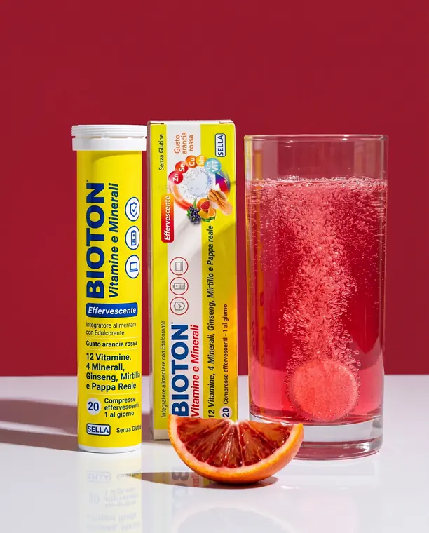 Tubo e confezione di Bioton Vitamine e Minerali effervescente con bicchiere di bevanda frizzante all'arancia rossa