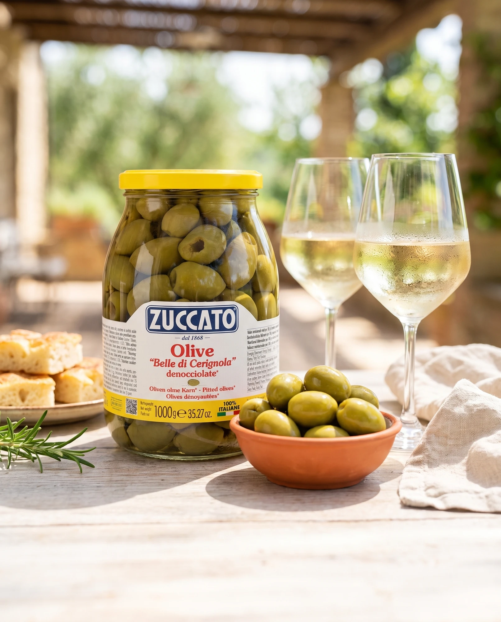Barattolo di olive Belle di Cerignola denocciolate Zuccato su tavolo all'aperto con bicchieri di vino bianco